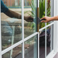 Two hands opening a glass door, with reflections and greenery visible outside