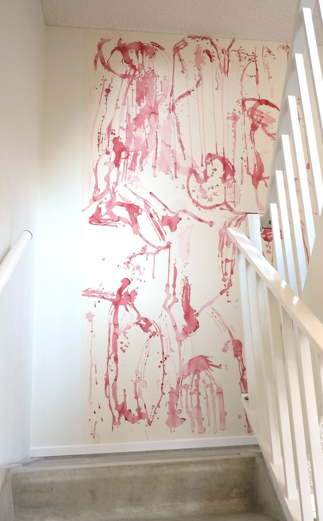 Een trappenhuis met een muur waarop een grote, abstracte muurschildering van rode verfspatten en -druppels op een witte achtergrond te zien is.