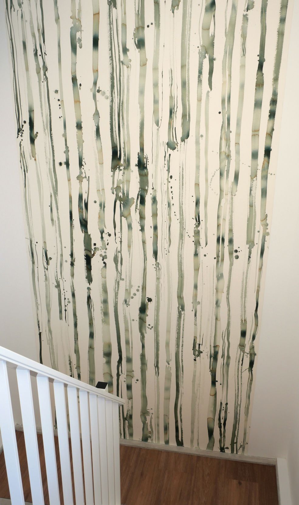 Een muur met een hoge, verticale muurschildering van gestileerde groen-zwarte berkenbomen boven een trappenplatform.