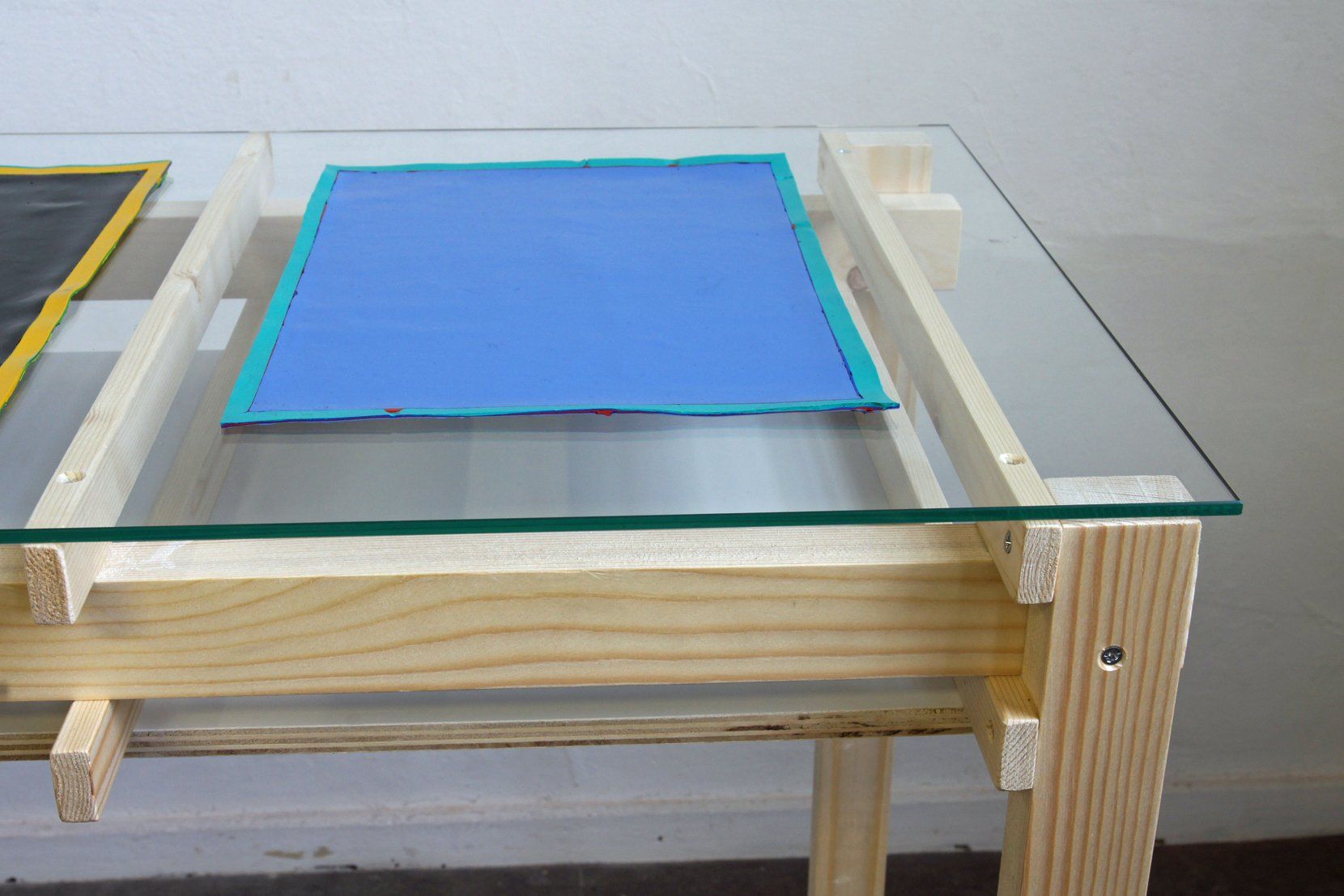 Een houten bijzettafel met een glazen blad, waarop in het midden een blauwe rechthoek is geplaatst.