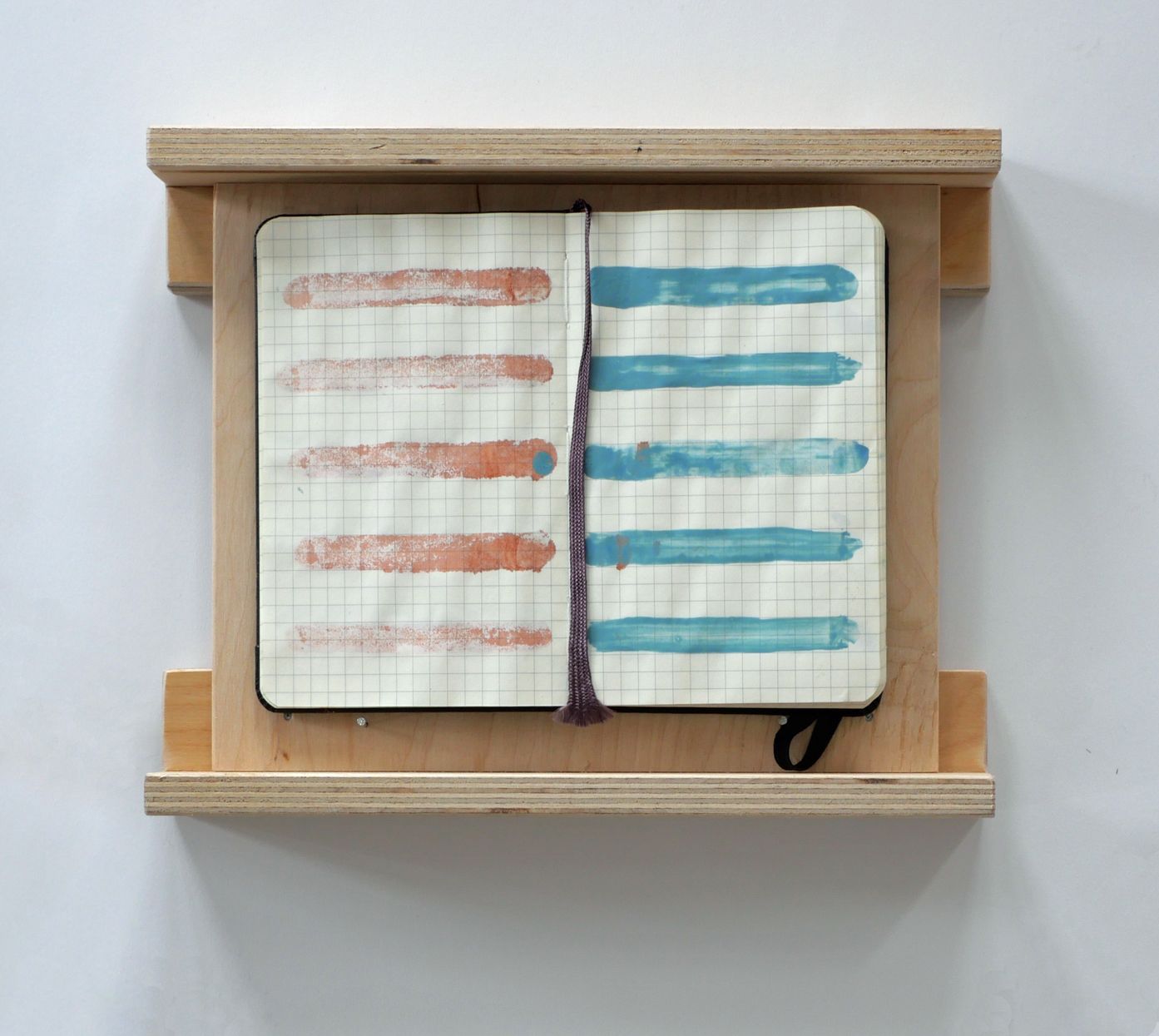 Een open notitieboek met horizontale rode en blauwe verfstrepen, tentoongesteld in een houten wandlijst.