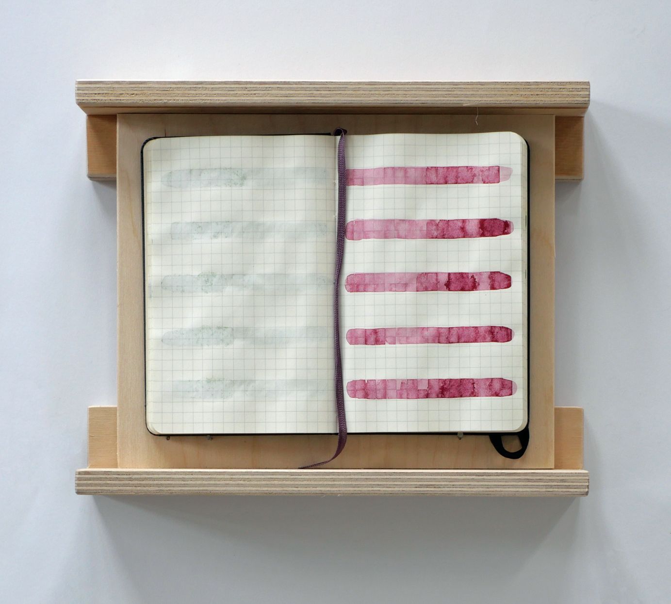 Een open notitieboek met rasterlijnen, ingelijst in een licht houten frame, met horizontale rode inktstalen op de rechterpagina.