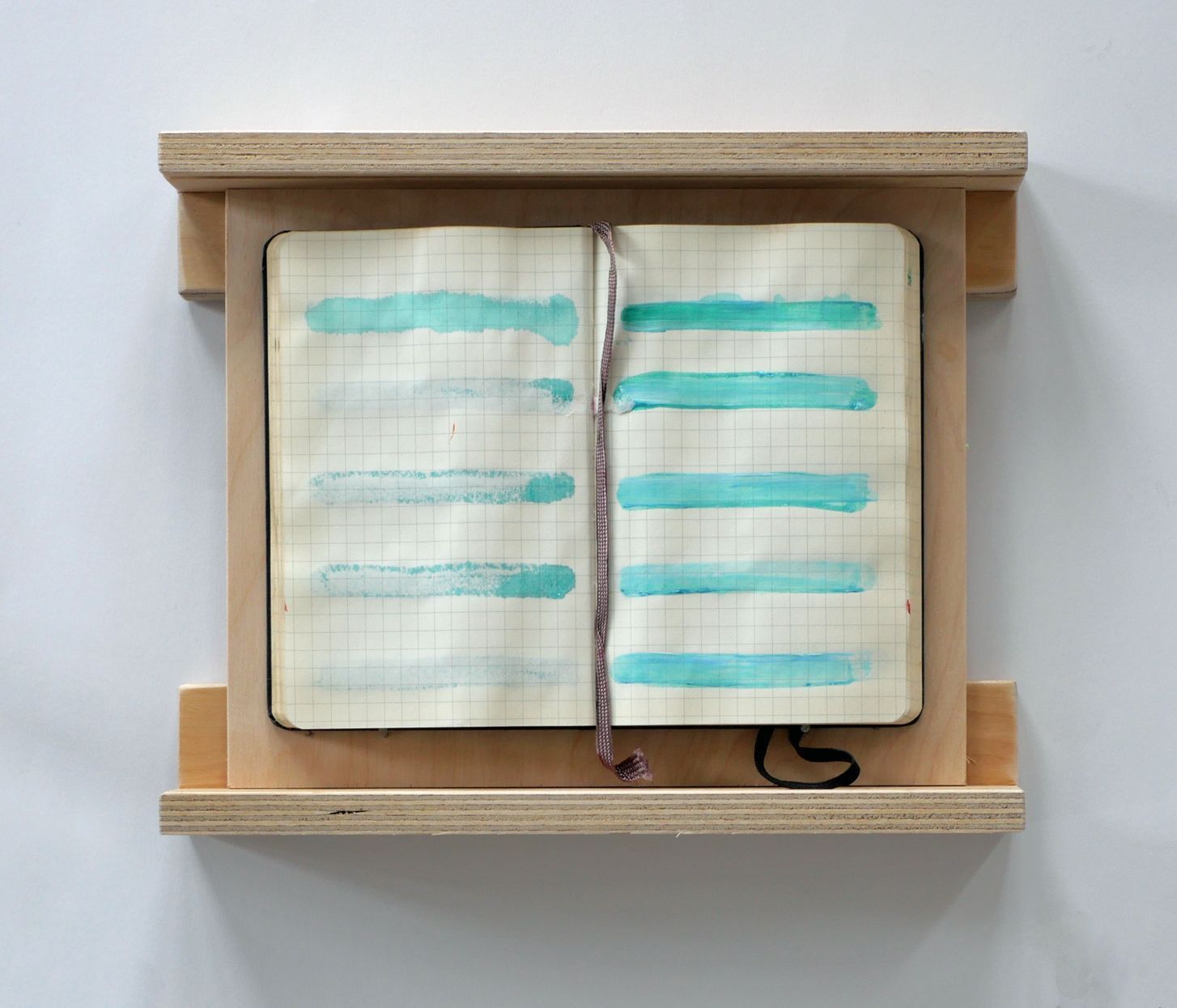 Een notitieboek met open rasterlijnen, ingelijst in een houten frame, met horizontale turquoise verfstrepen over de pagina's.