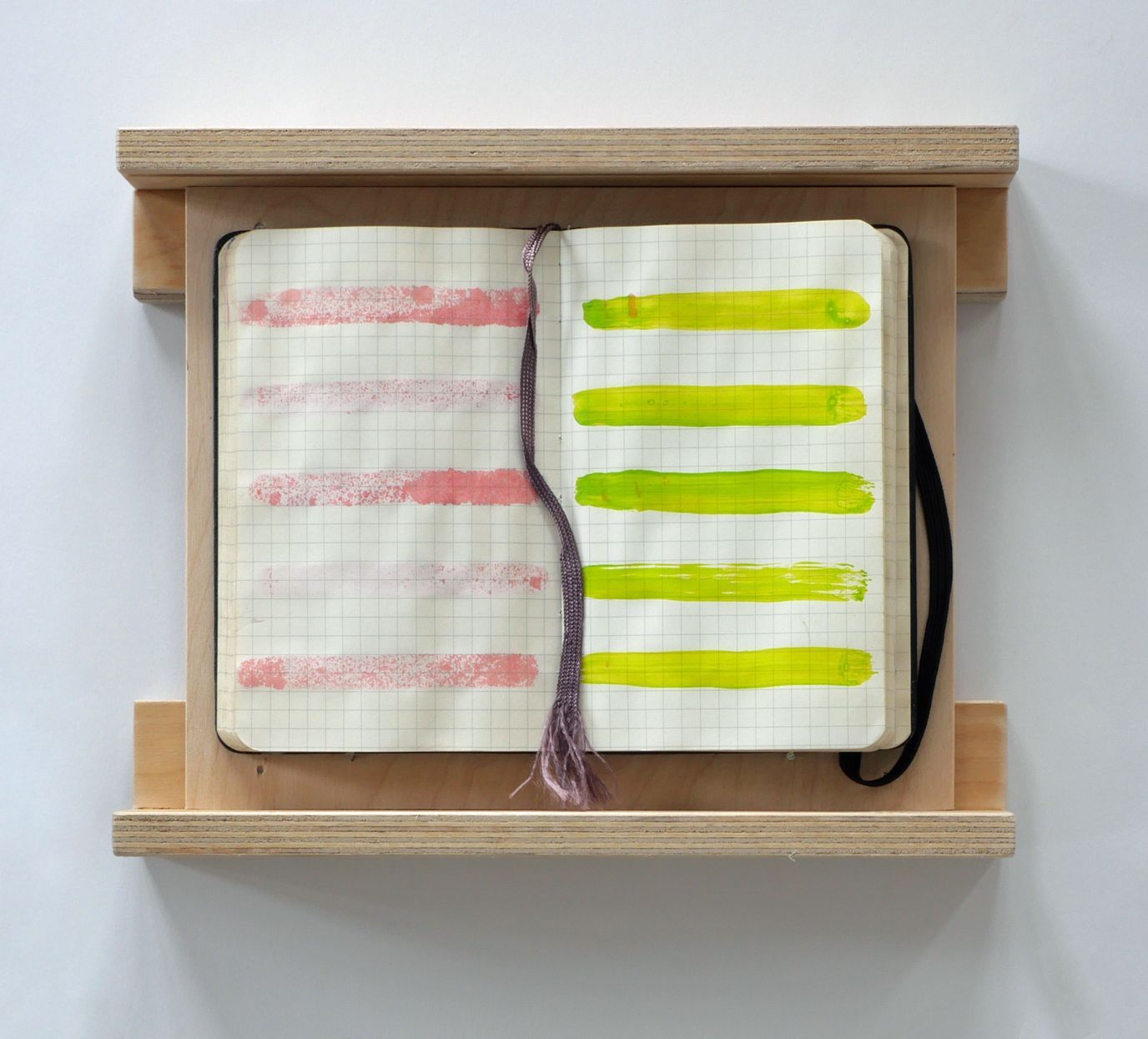 Een open notitieboek, ingelijst in een houten frame, met vijf horizontale roze strepen aan de linkerkant en vijf groene strepen aan de rechterkant.