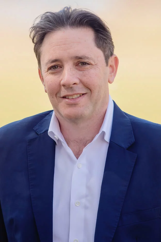 A man in a blue plaid shirt is standing with his arms crossed.