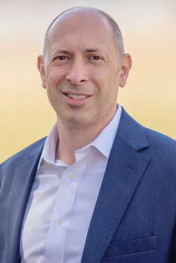 A man in a suit and white shirt is smiling for the camera.