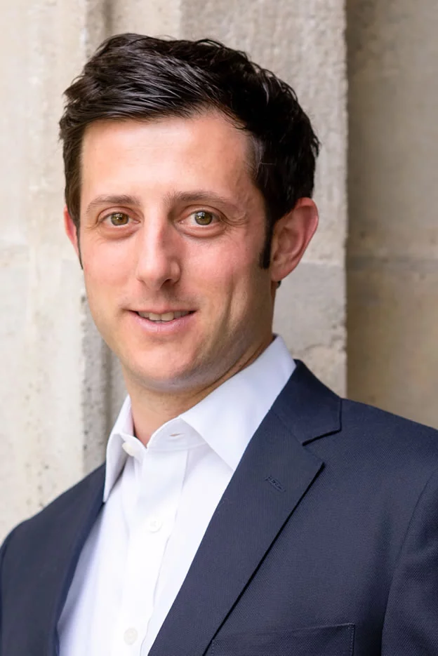 A man in a blue shirt and black pants is standing with his hands in his pockets.