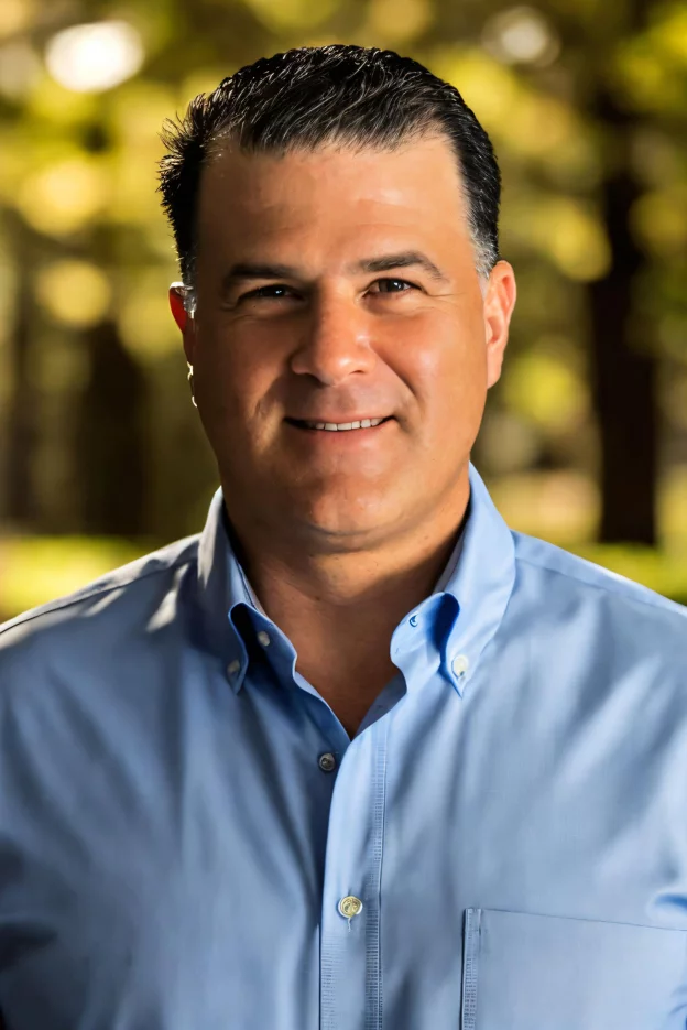 A man in a blue shirt and black pants is standing with his hands in his pockets.
