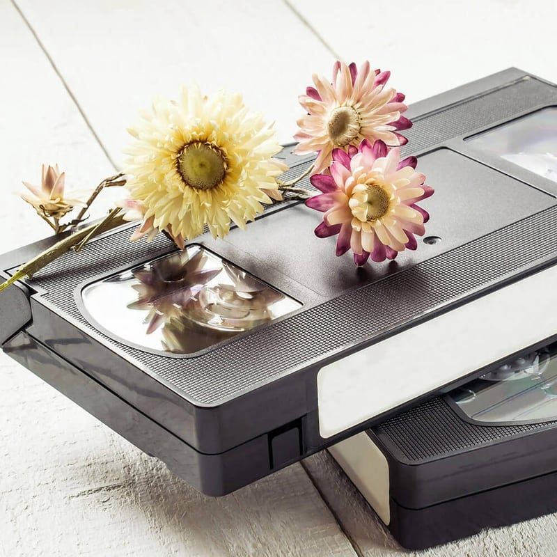 Two stacked VHS tapes with flowers resting on top, in a bright studio setting