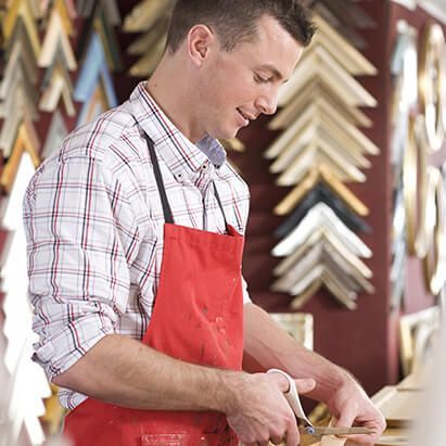 Person in a red apron using scissors to cut material in a framing shop