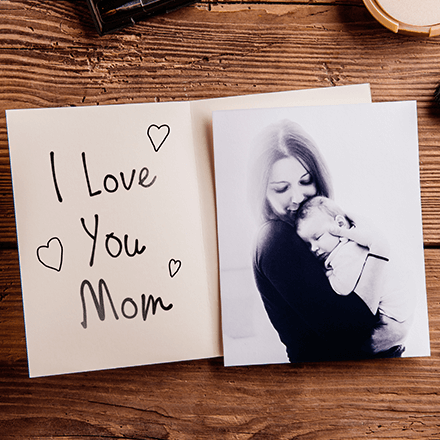 Handwritten “I Love You Mom” beside a black-and-white mother holding baby on a wooden table