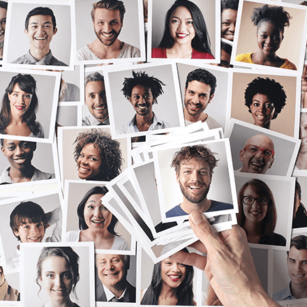 Hand holding a fan of portrait photos scattered among smiling headshots on a white background
