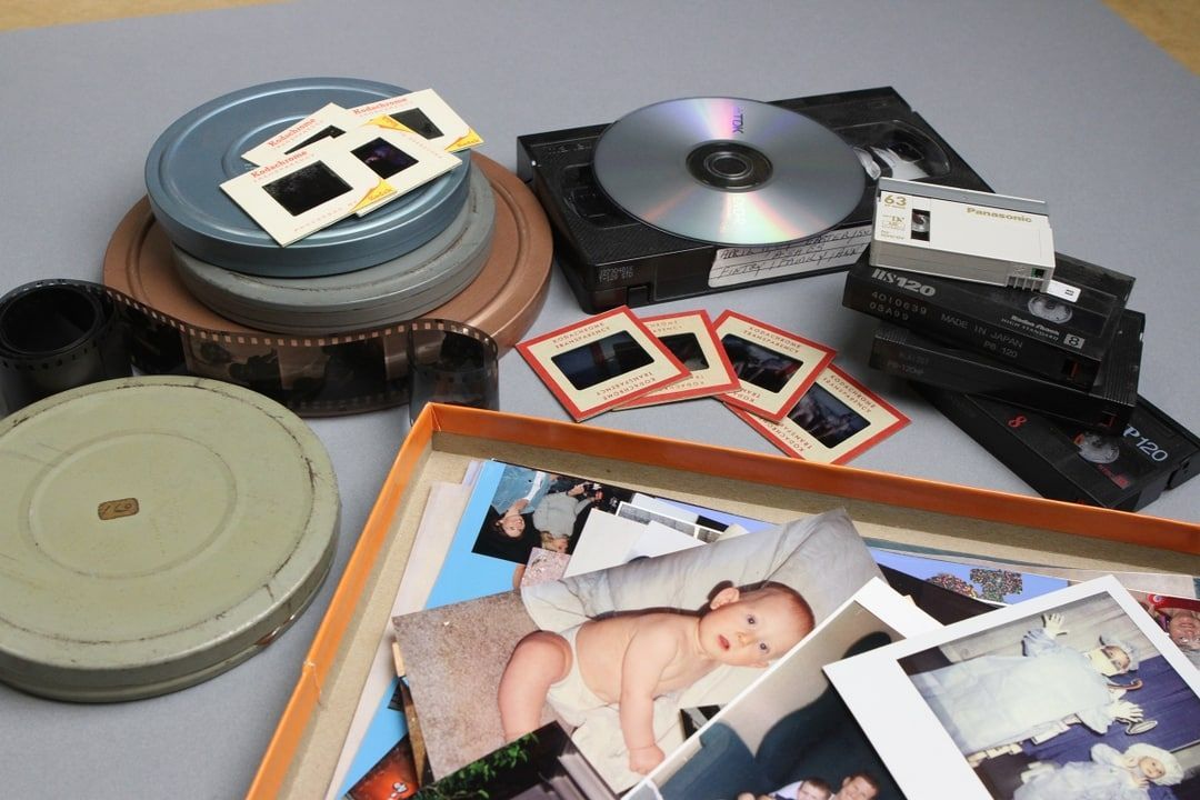 Scattered photo prints, film reels, and slides on a table with a baby photo in the foreground