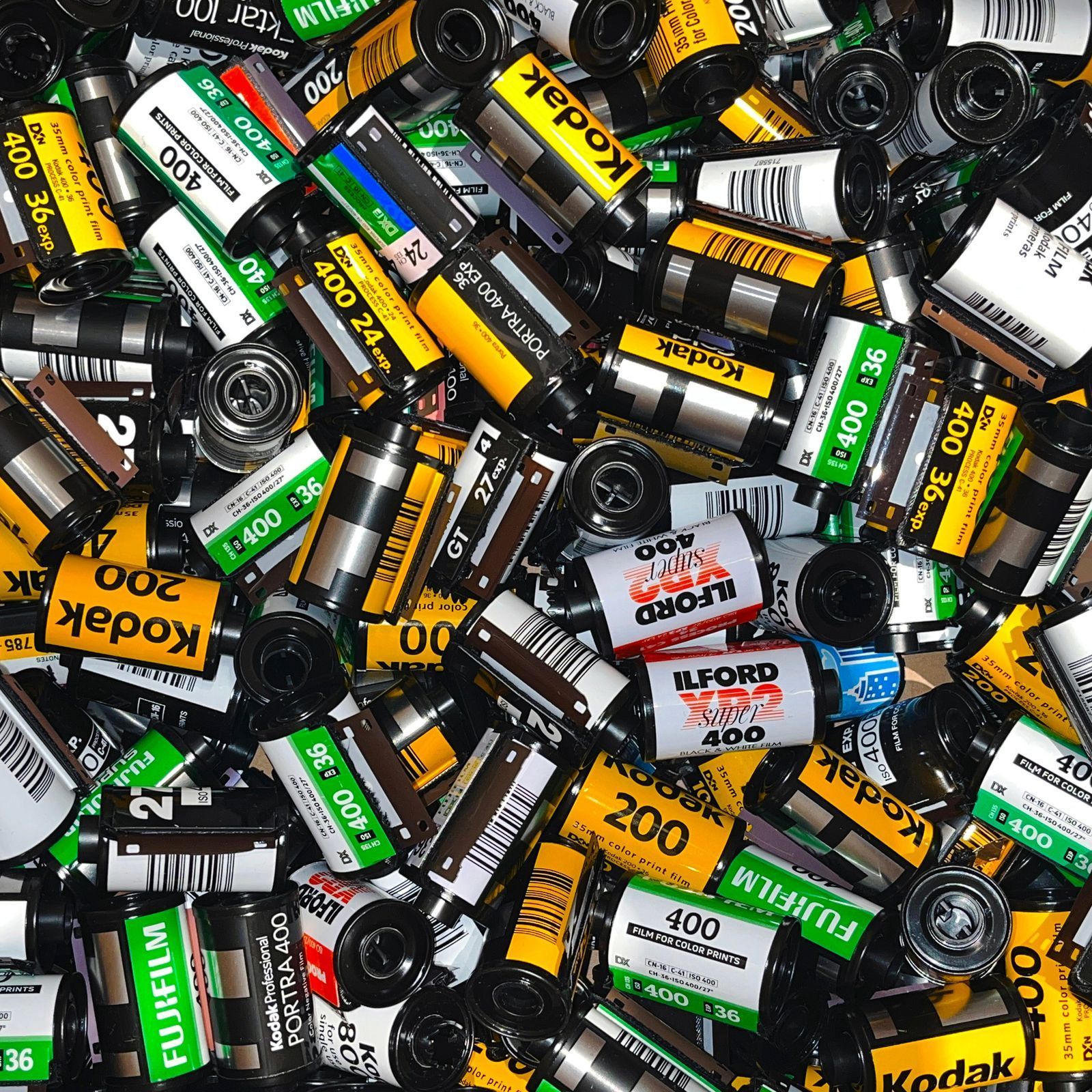 Scattered rolls of Kodak and Fujifilm 35mm film cartridges in black, white, yellow, and green labels
