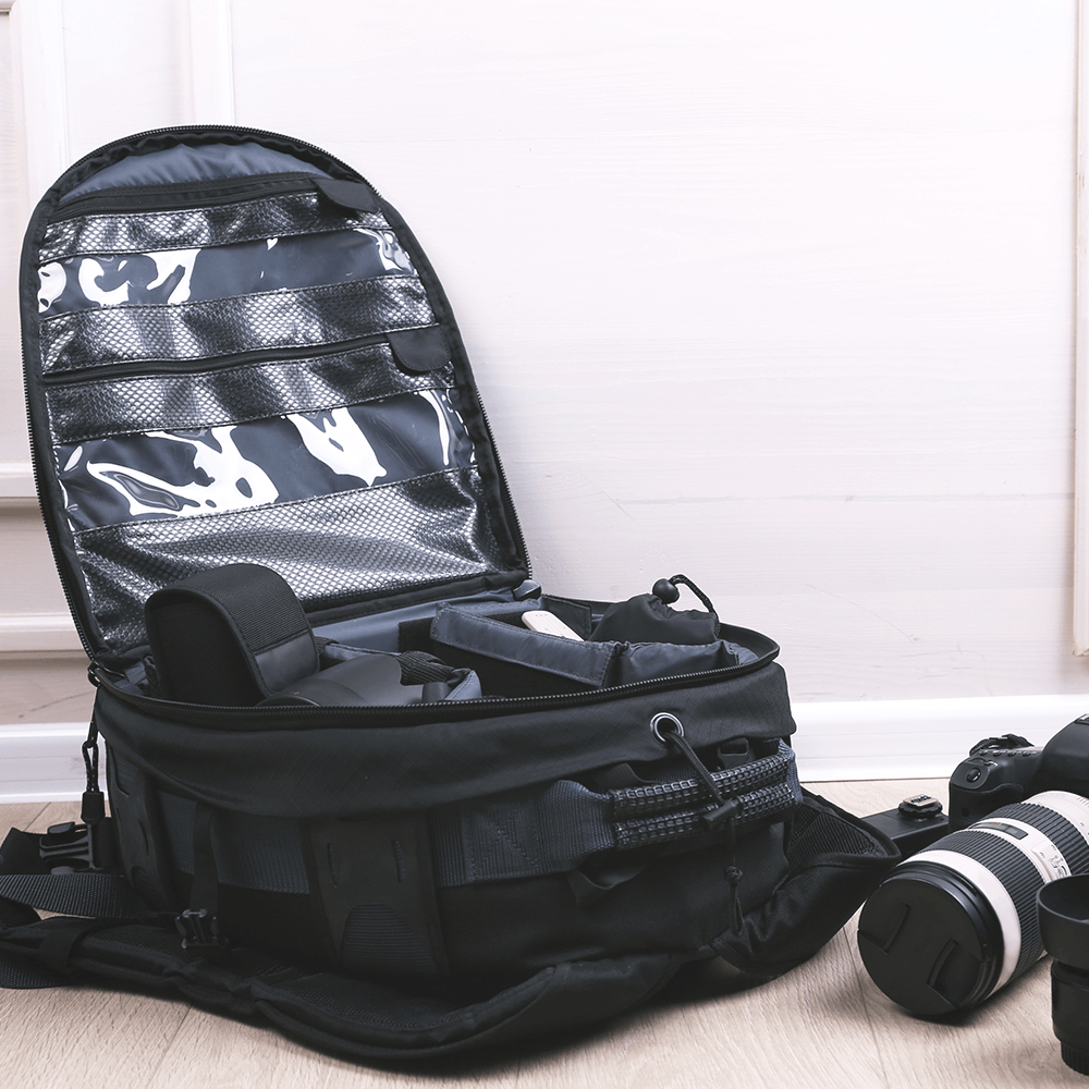 Open black camera bag with compartments beside a striped camera lens on a light floor