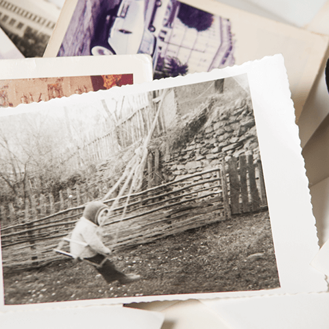Black-and-white photo of a person crouching by a fence in a wooded outdoor area