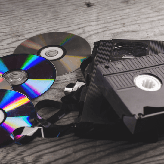 Stacks of black VHS tapes and colorful CDs scattered on a wooden surface