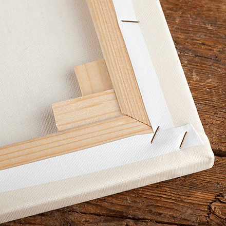 Close-up of a framed canvas corner with wooden stretcher bars on a wooden table.