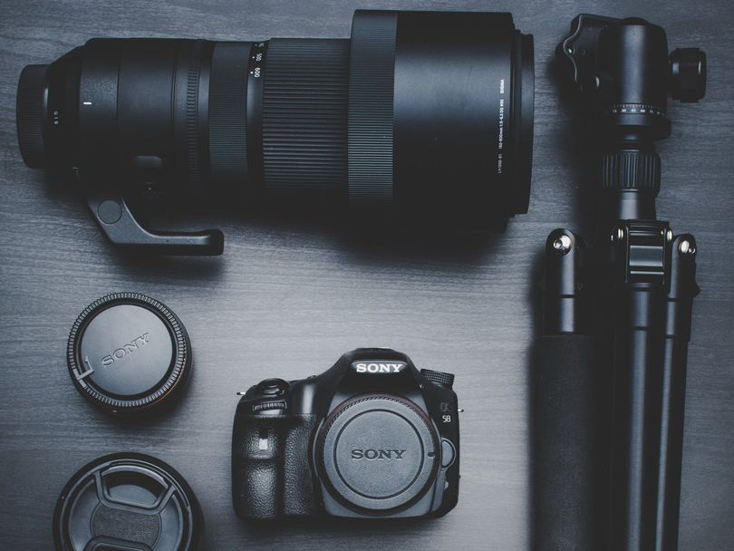 Camera gear laid out on a gray surface: DSLR, telephoto lens, and tripod attachments