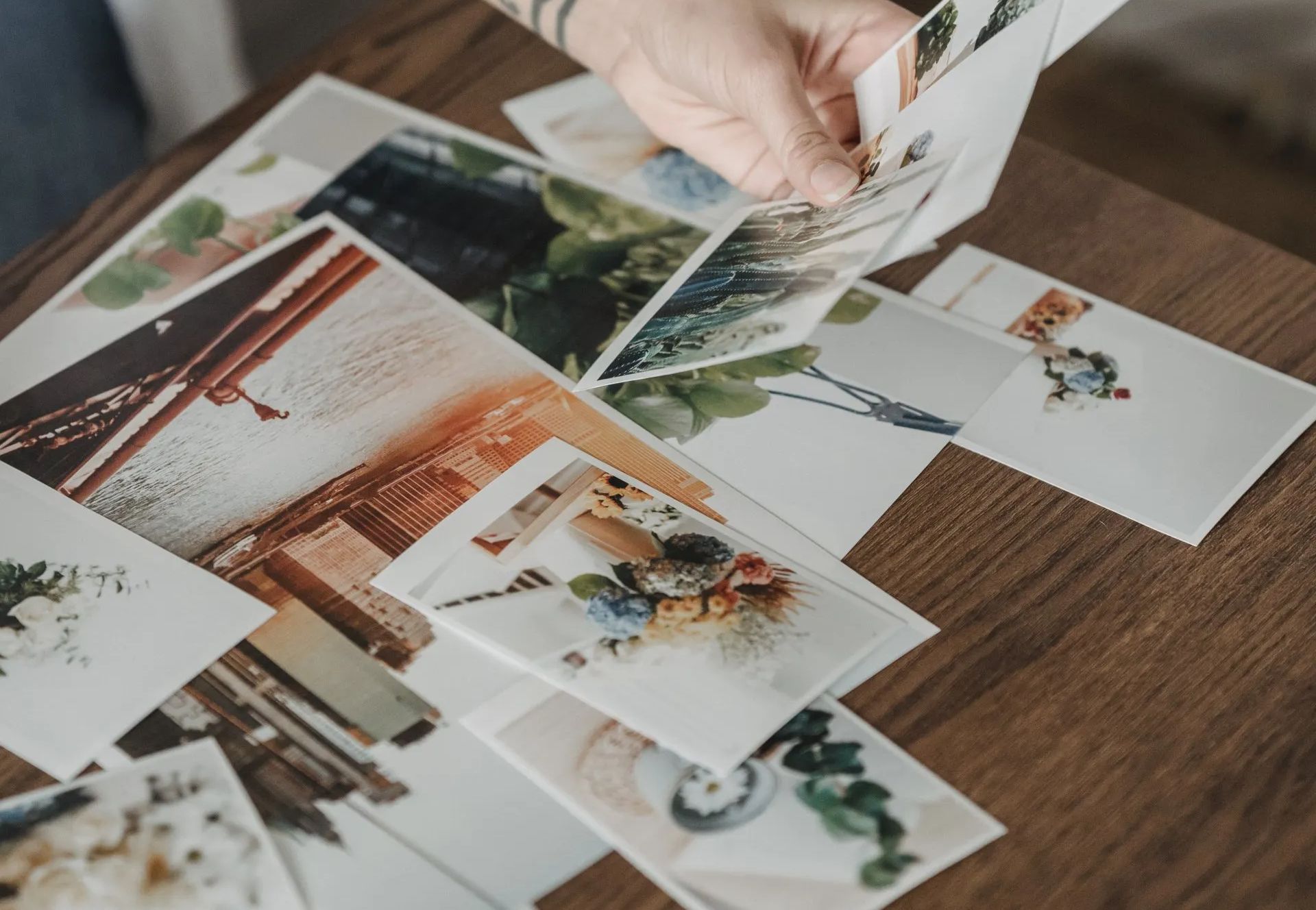 Hand placing printed photos on a wooden table, including landscapes and a wedding scene