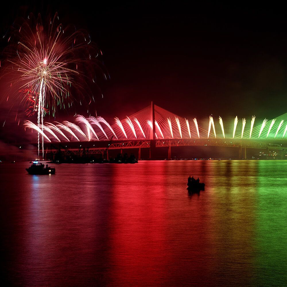 Fireworks lighting a bridge at night, with red, white, and green reflections on the water.