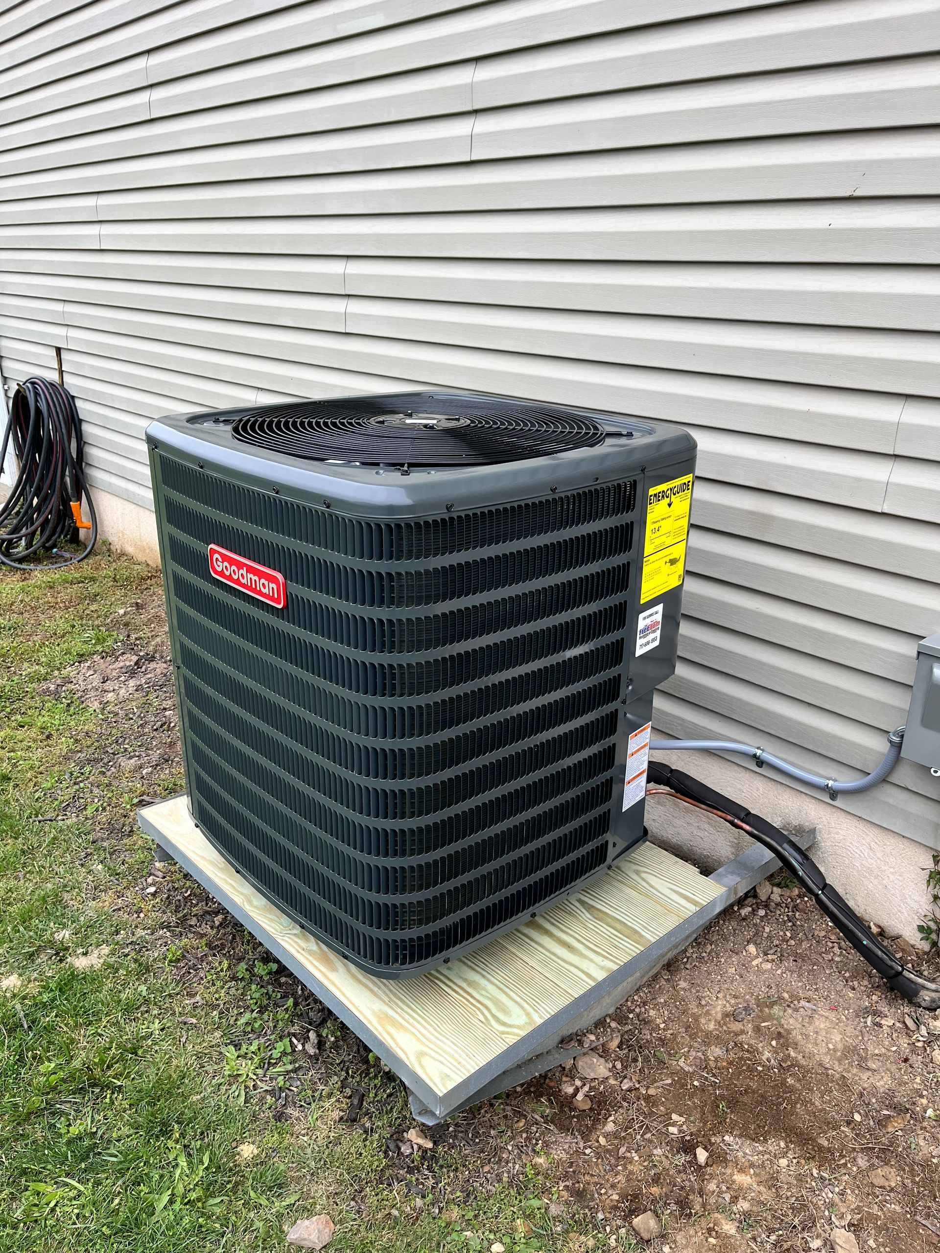 Air conditioner unit on a wooden platform next to a house with gray siding.