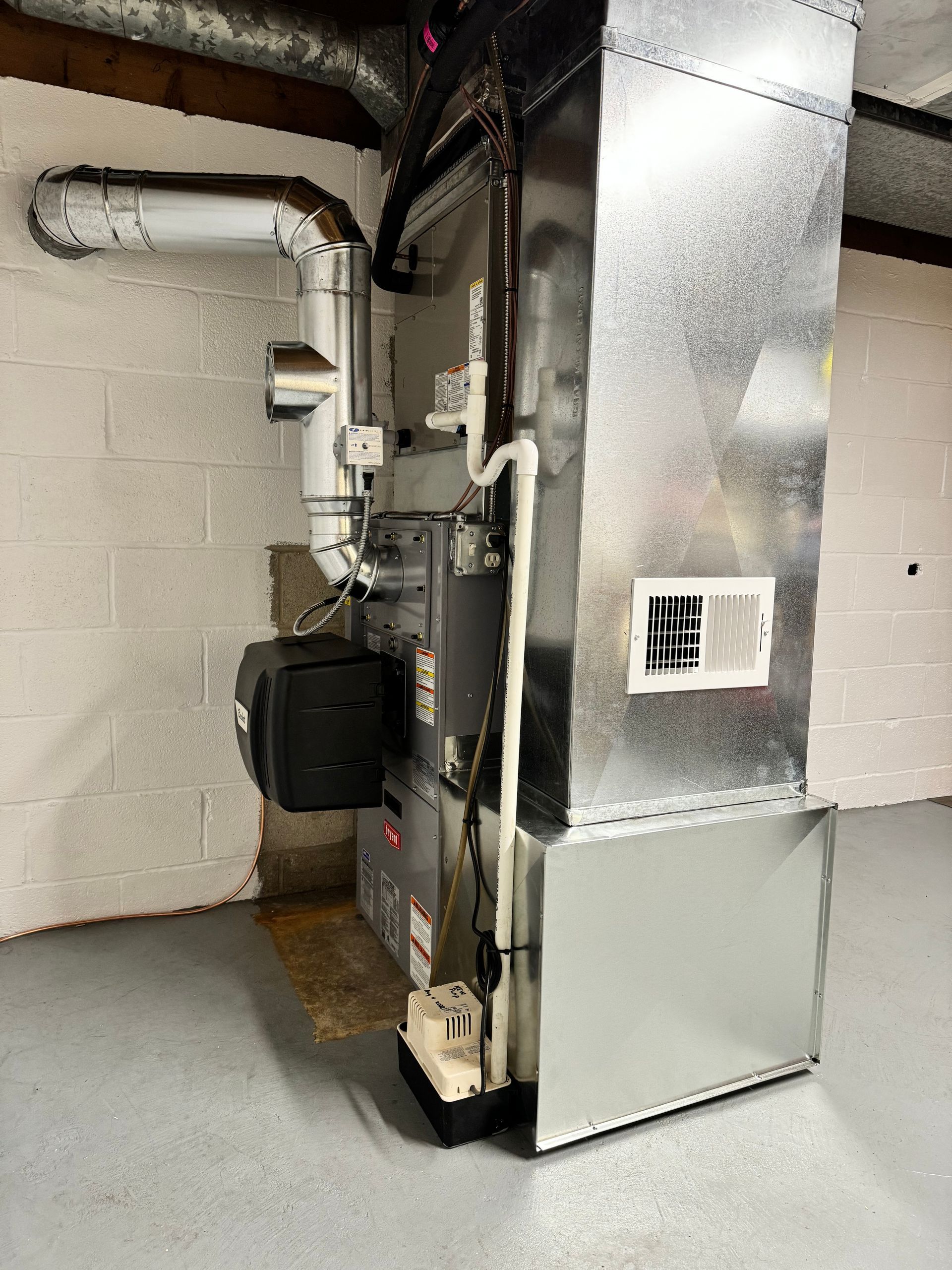 Furnace with metal ductwork against a white painted wall in a basement.