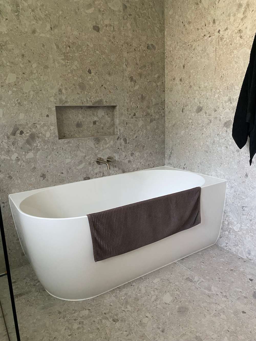 A Sleek White Bathtub Against Speckled Gray Stone Walls and Floor — Nick Hall Builder in Cooroy, QLD