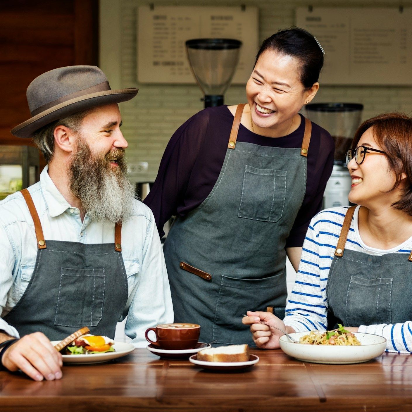 A group of people wearing aprons are sitting at a table with food.