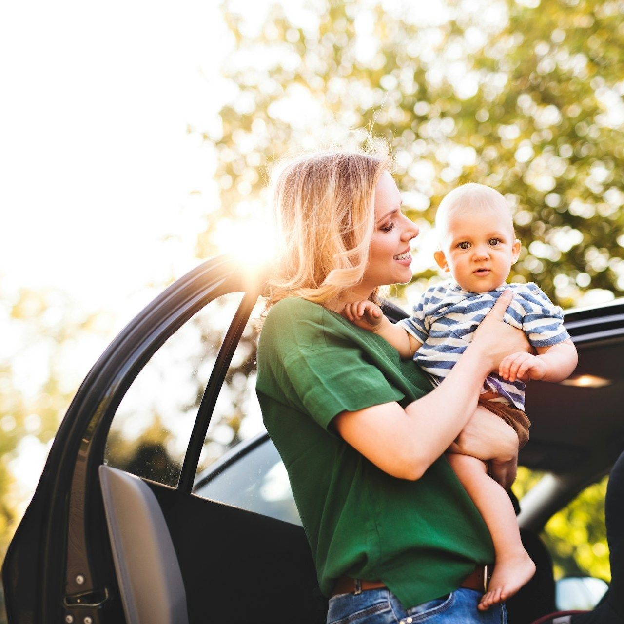 A woman is holding a baby in front of a car.