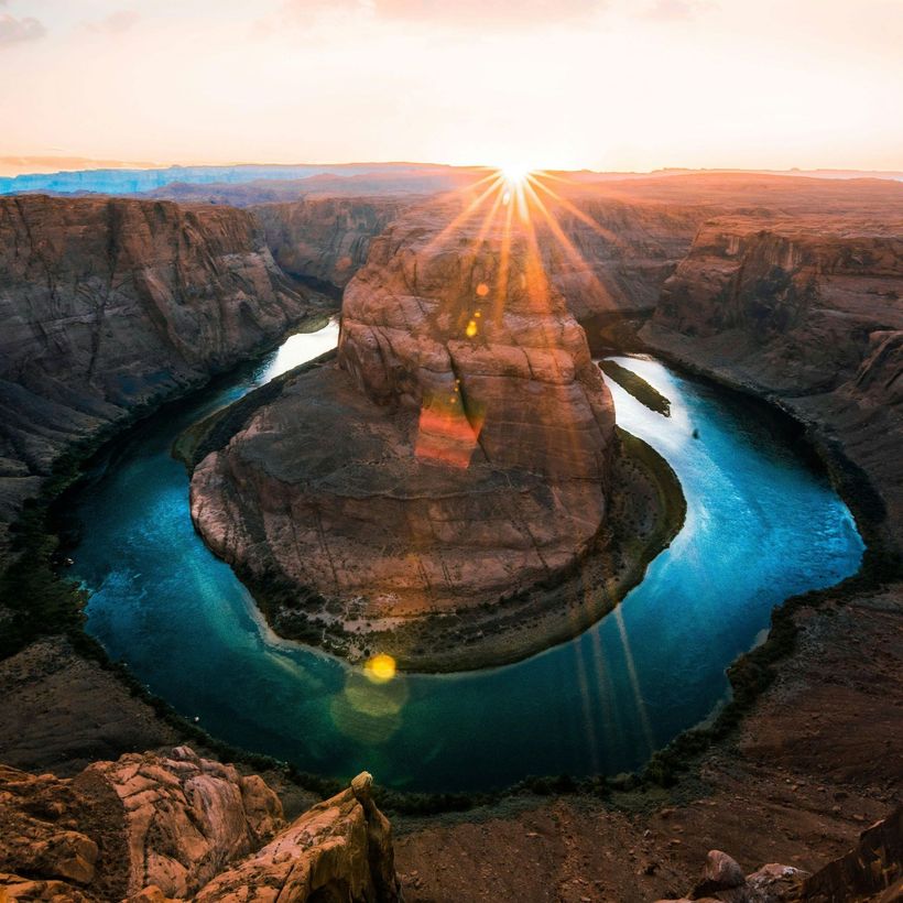 The sun is shining through the clouds over a river surrounded by rocks.