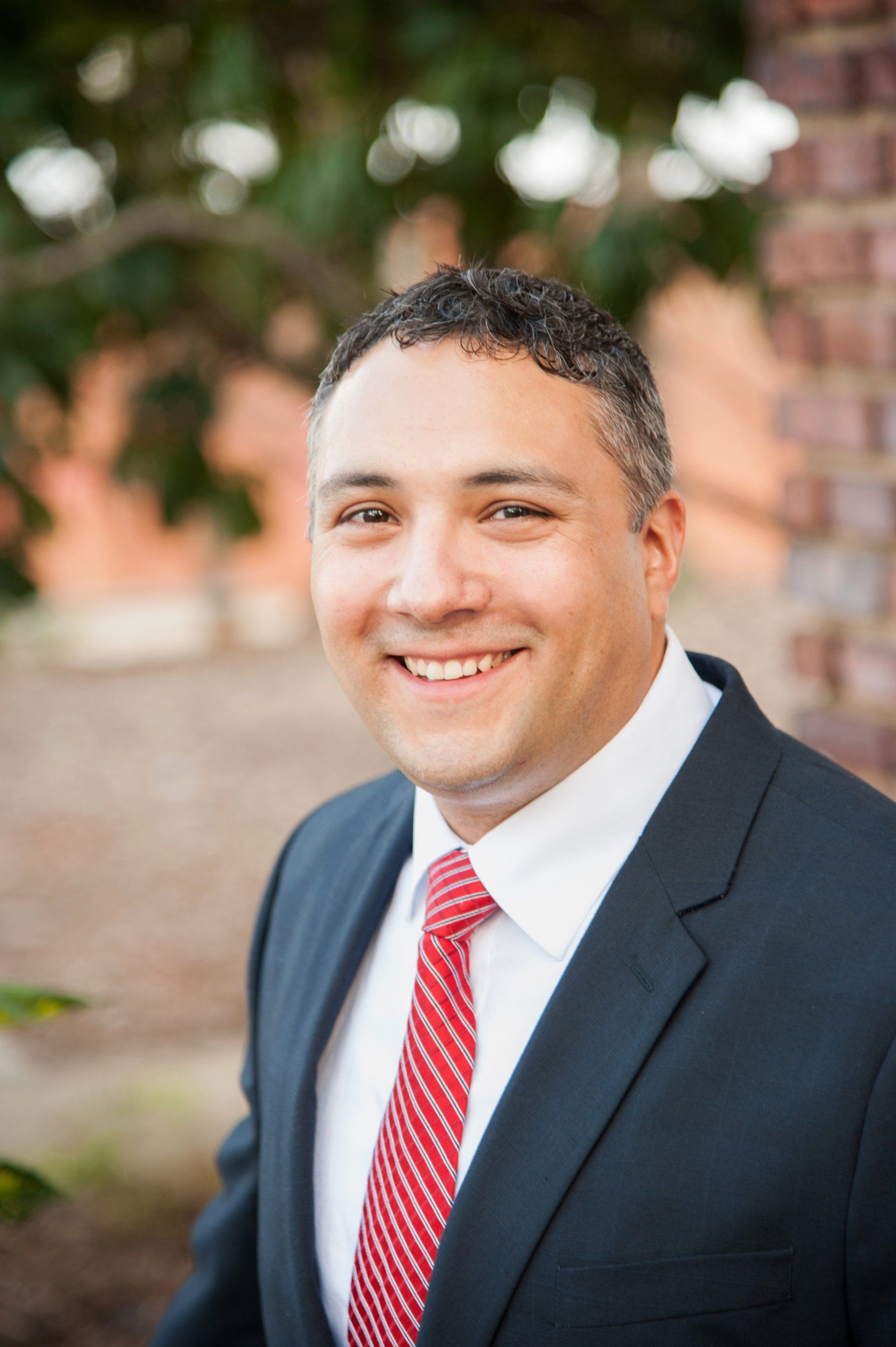 A man in a suit and tie is smiling in front of a brick wall.