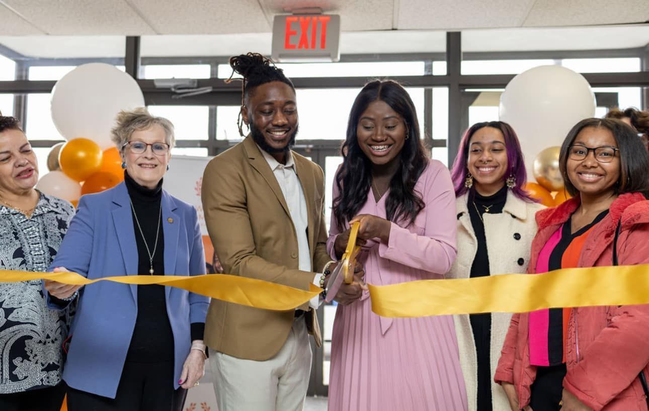 A group of people are cutting a yellow ribbon.