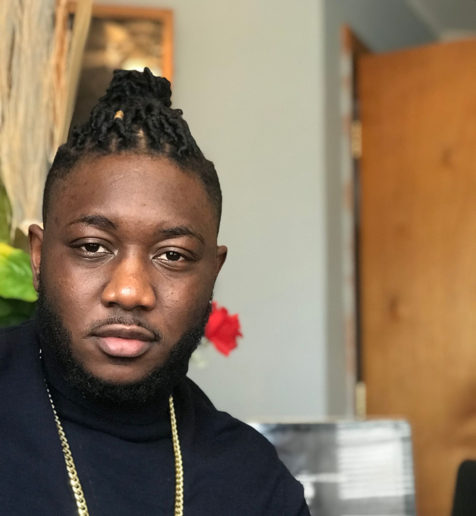 A man with dreadlocks and a turtleneck looks at the camera