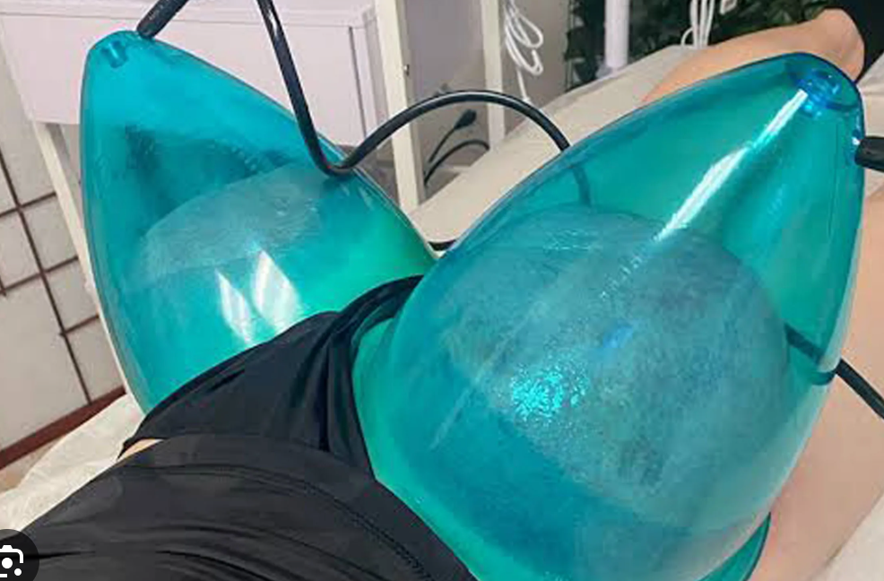 A woman is laying on a bed with two blue balloons on her chest.