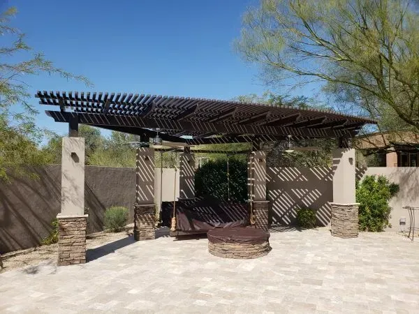 Stone patio with a wooden pergola and bench in a sunny outdoor courtyard