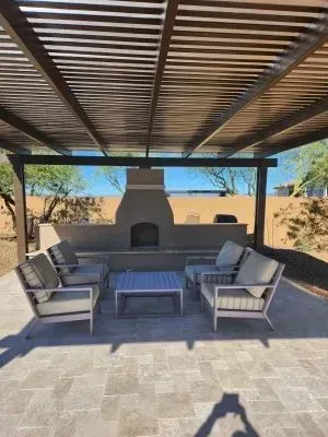 Covered patio with outdoor seating and a central fireplace overlooking a sunlit yard.
