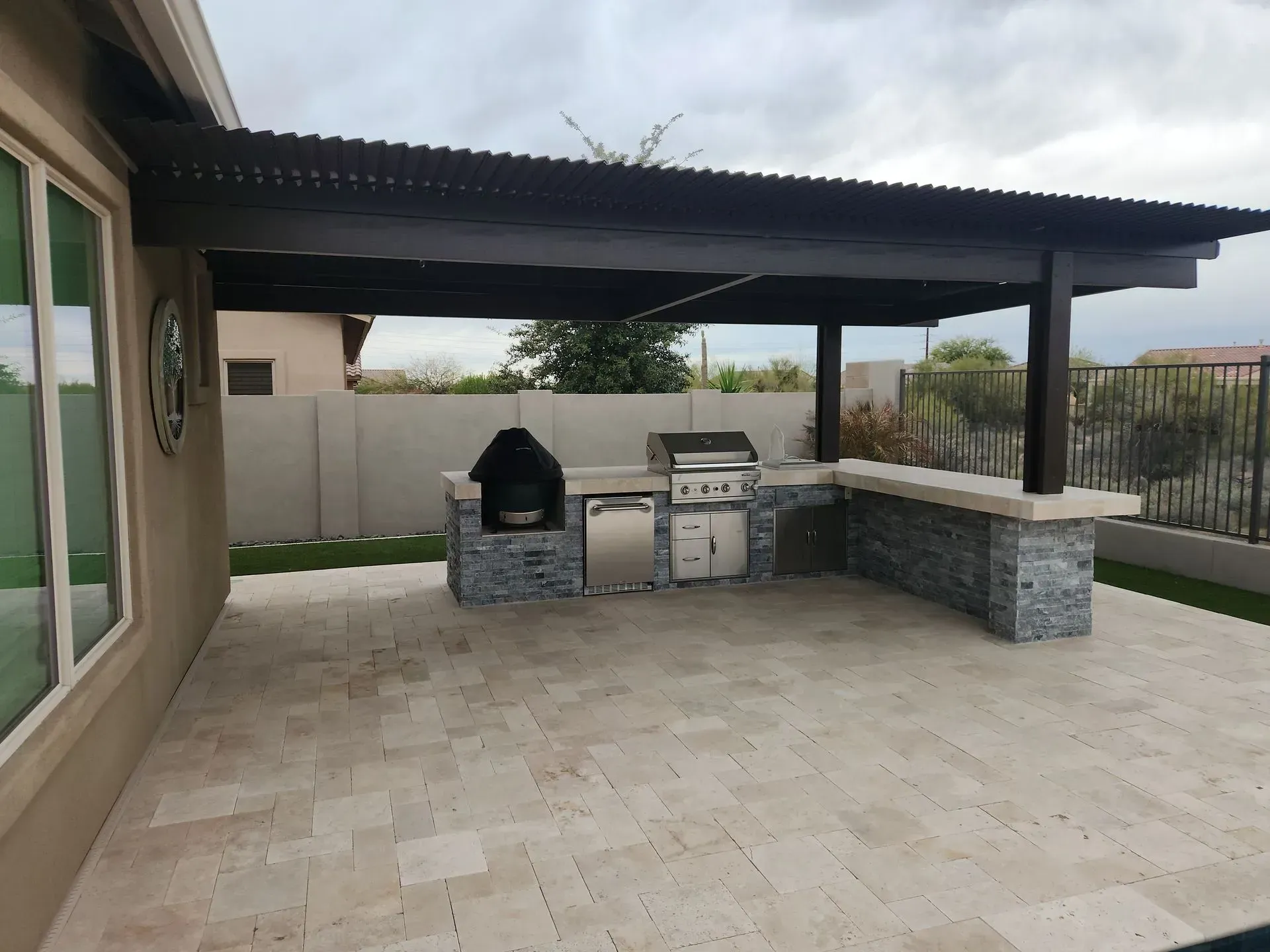 Covered outdoor patio with a built-in grill, stone counters, and tiled flooring under a dark roof