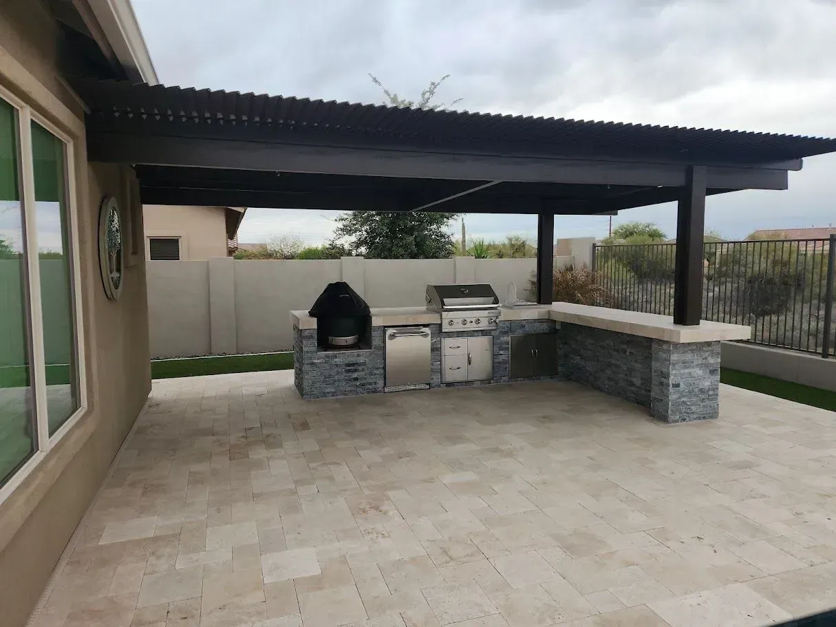 Covered patio with outdoor grill and stone counter on a tiled backyard terrace