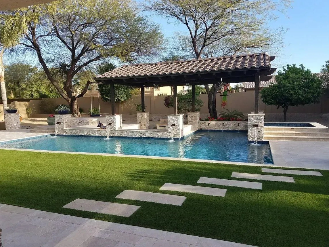 Backyard pool with a shaded pavilion, lawn, stone path, and trees under a clear blue sky