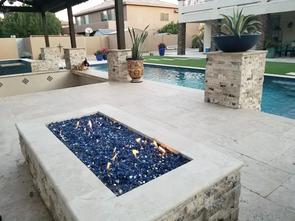 Backyard patio with a blue-tiled fire pit beside a swimming pool and stone planters