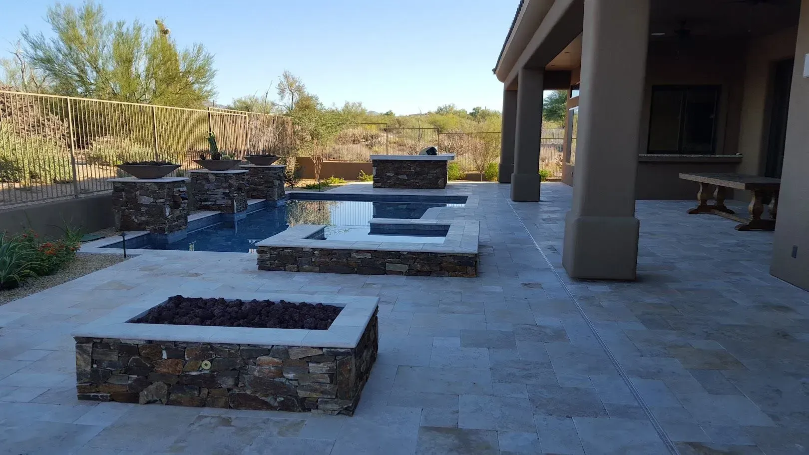 Back patio with stone pavers, rectangular fire pit, and low seating walls beside a house