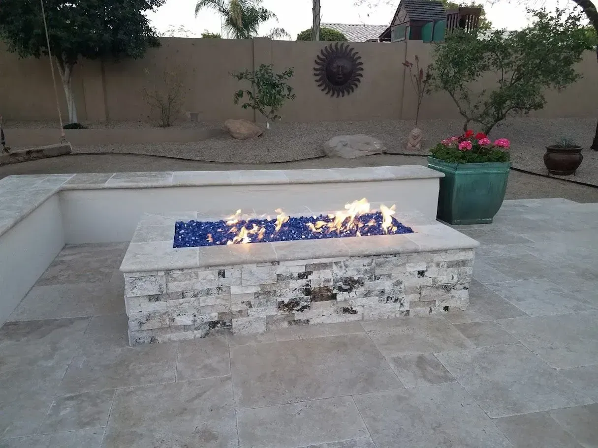 Modern patio with a lit rectangular fire pit and potted plants at dusk