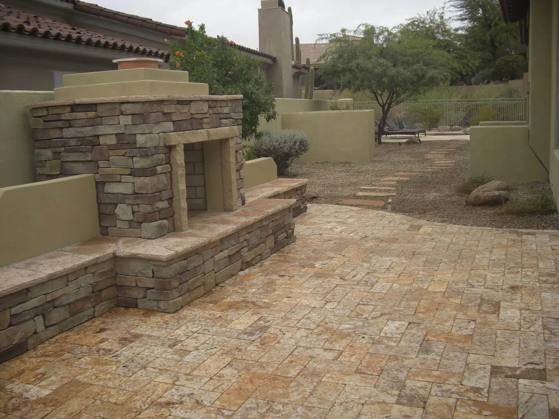 Stone-paved courtyard with a built-in stone fireplace and beige walls in a desert-style home setting