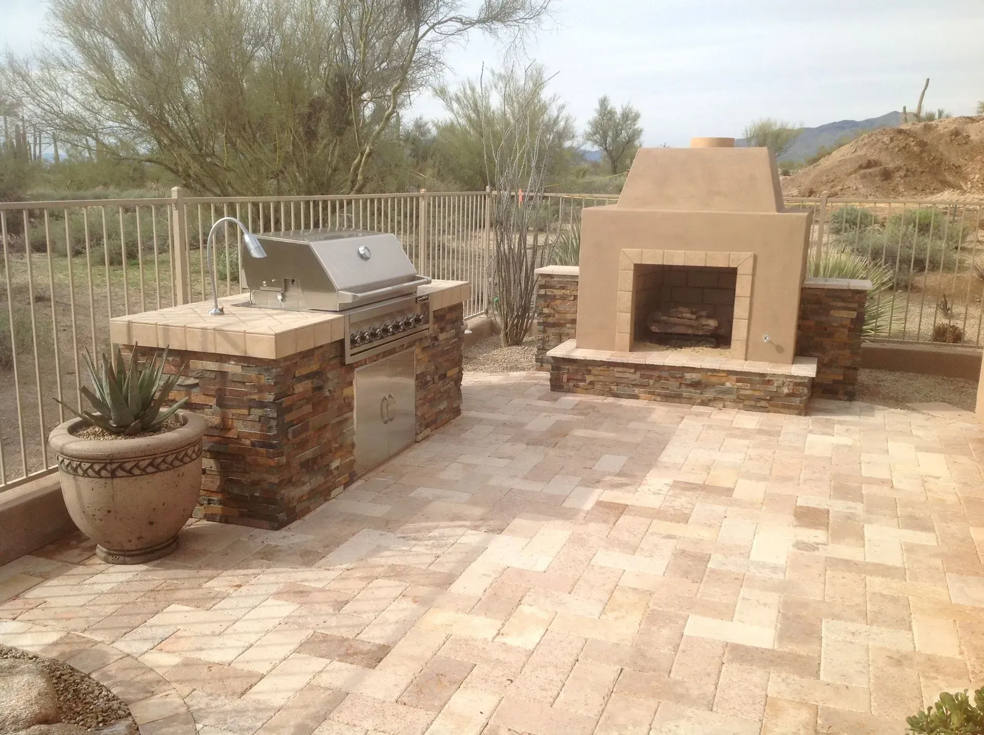 Outdoor patio with brick grill and tan outdoor fireplace on a paved terrace