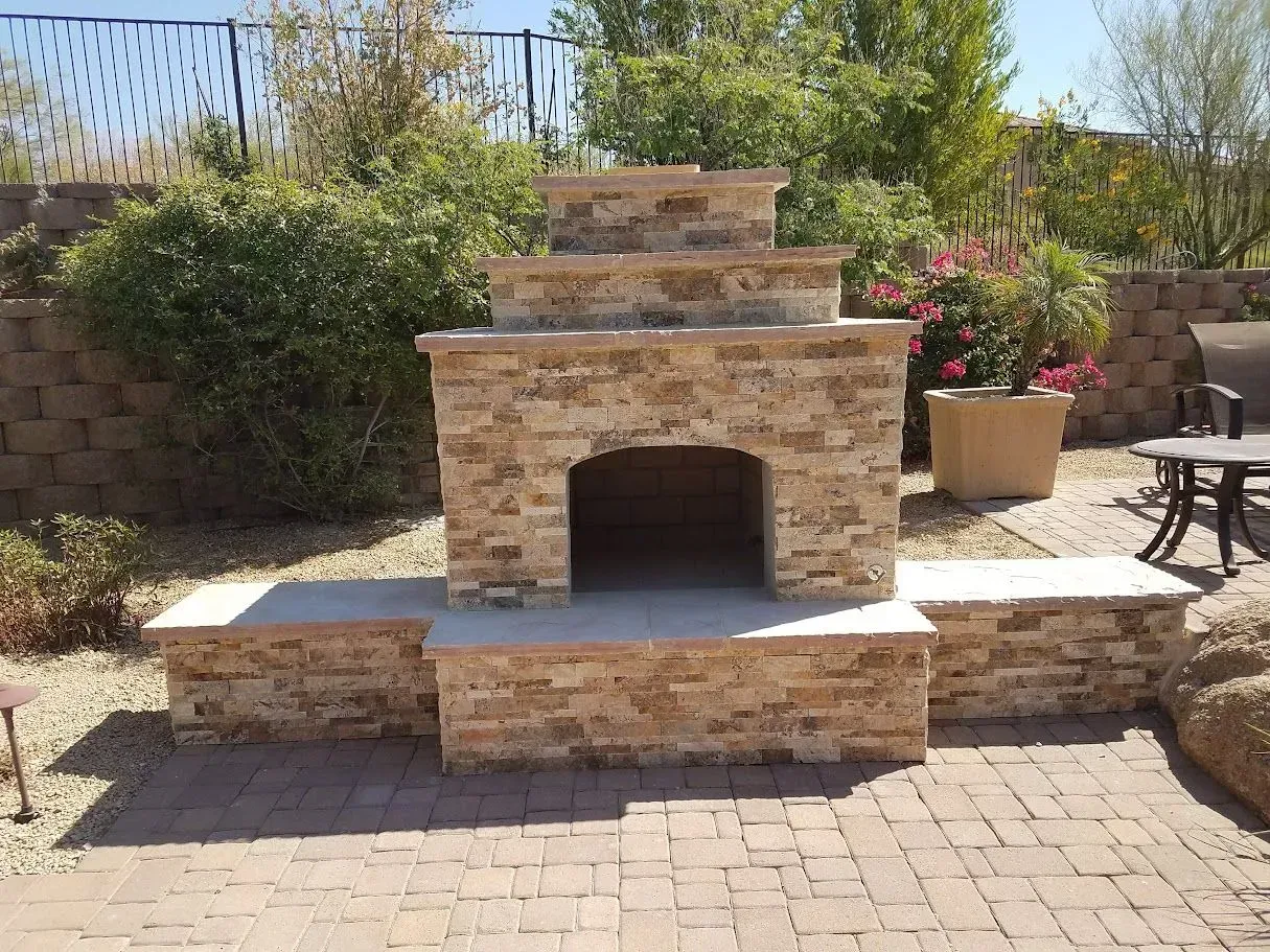 Backyard stone fireplace with built-in bench seating on a brick patio, surrounded by plants