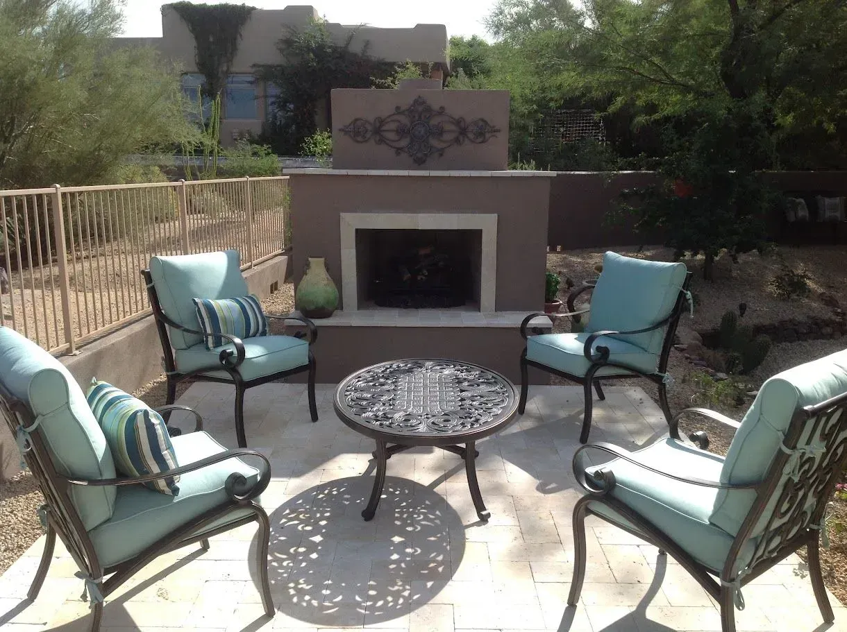 Outdoor patio with four turquoise chairs around a round metal table and a fireplace in the background