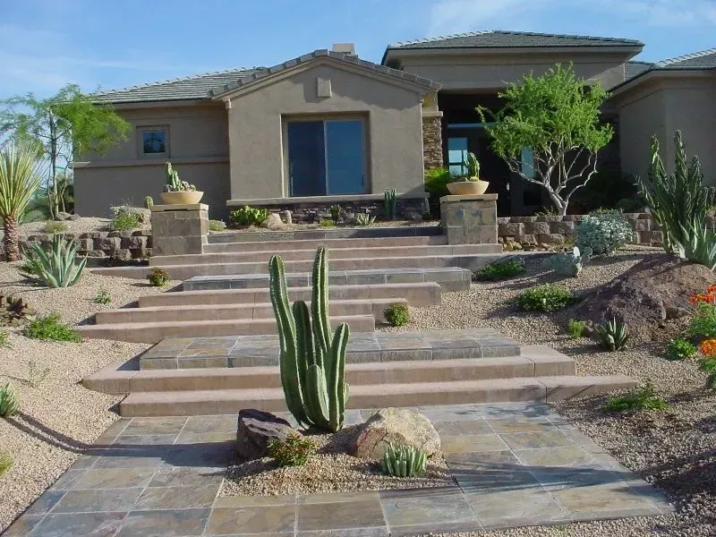 Desert home with front steps, stone planters, and cacti in a landscaped yard