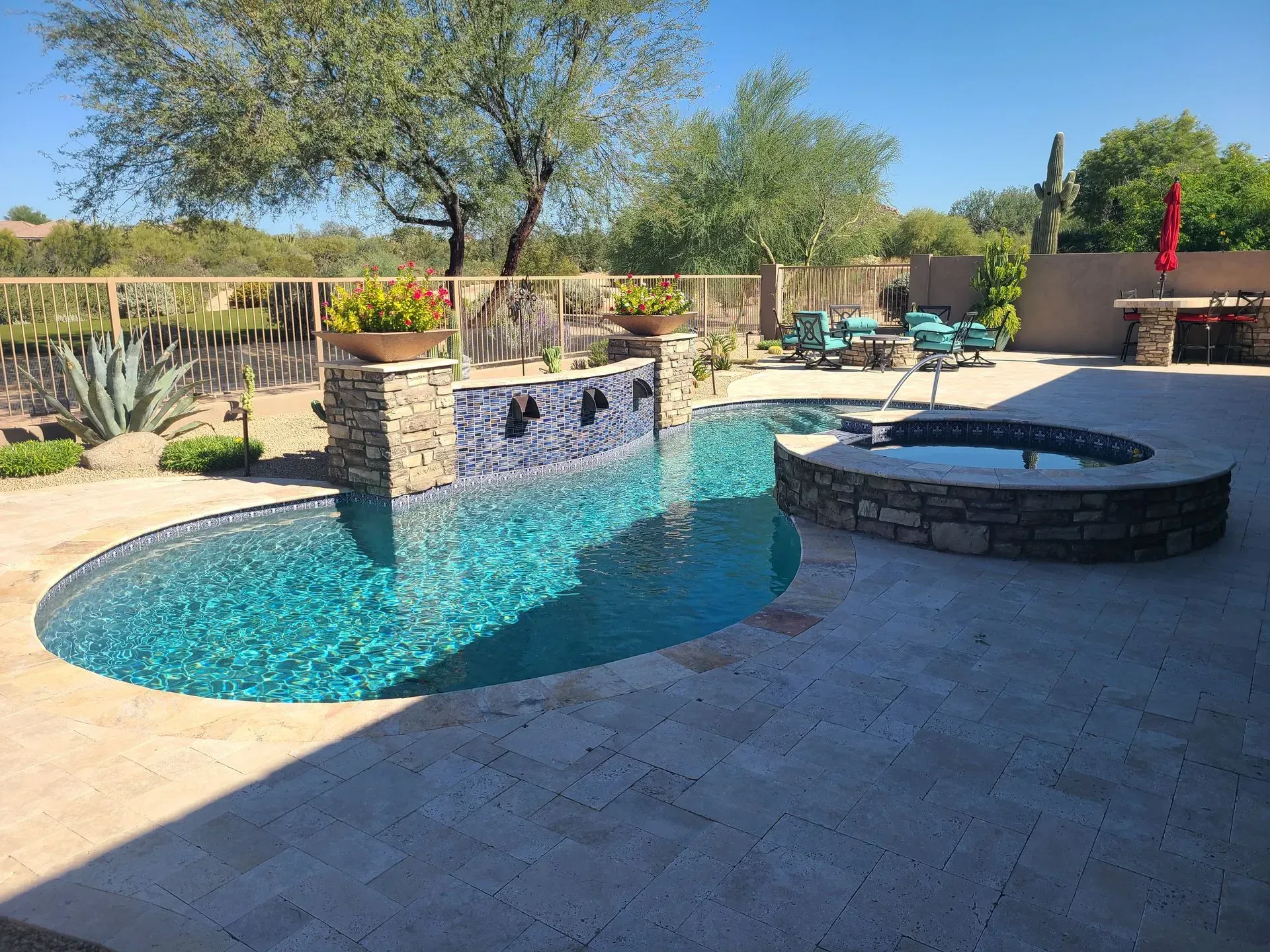Backyard pool with turquoise water, stone waterfall, hot tub, and patio under a sunny sky