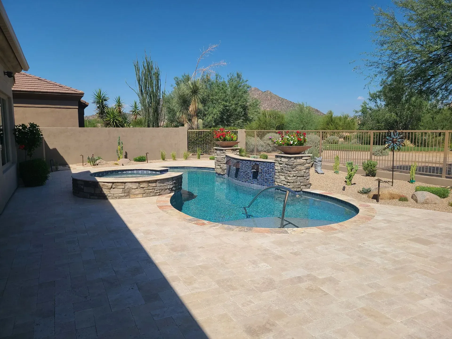 Backyard patio with a blue pool, stone spa, and desert landscaping under a clear sky